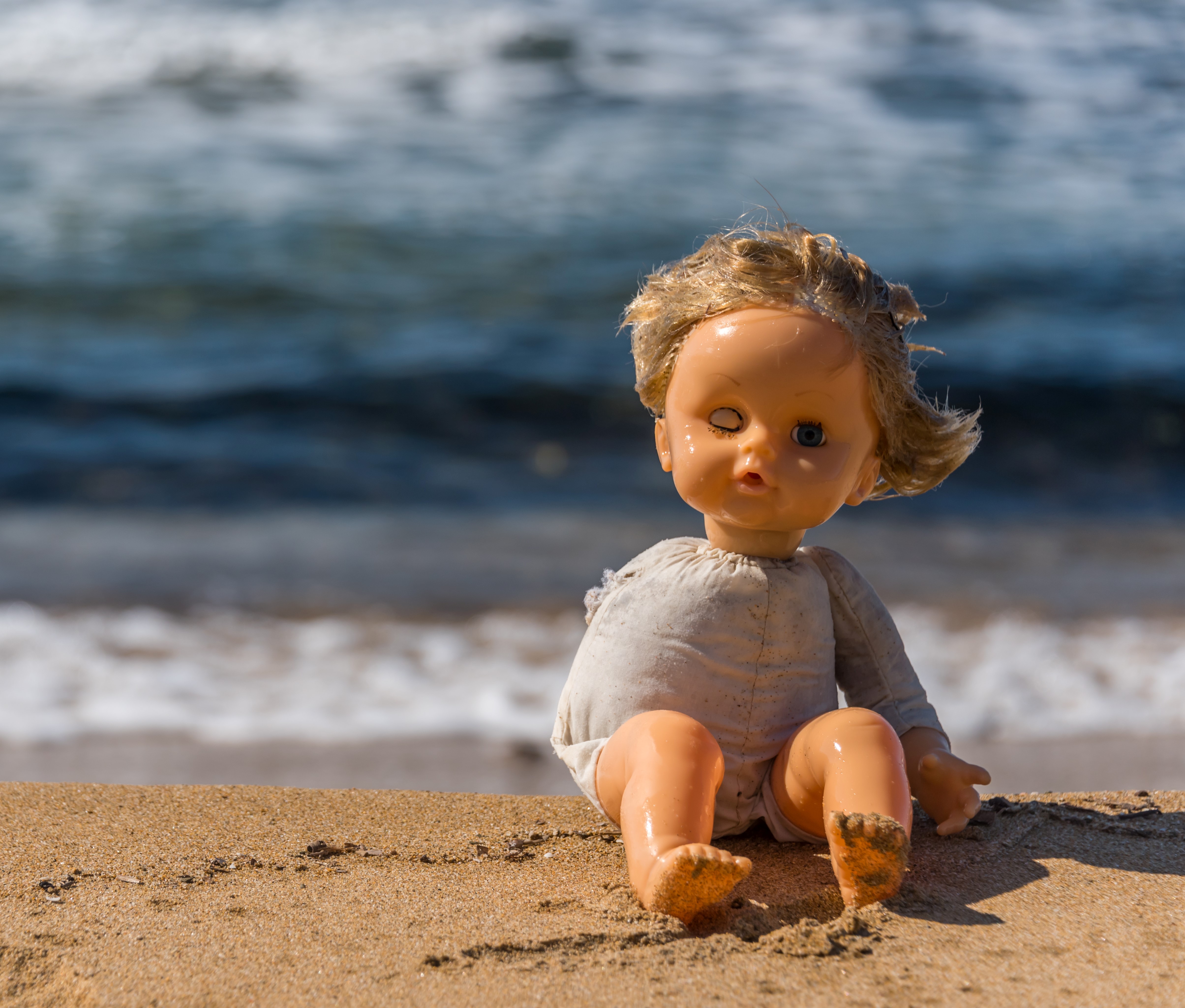 Old Broken Toy Doll Sitting on a Beach in Italy